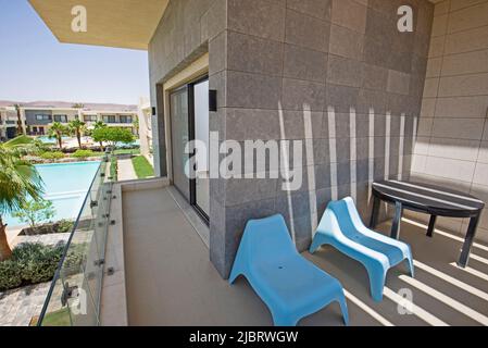 Terrace furniture at a luxury apartment in tropical resort with table and chairs on balcony and swimming pool view Stock Photo