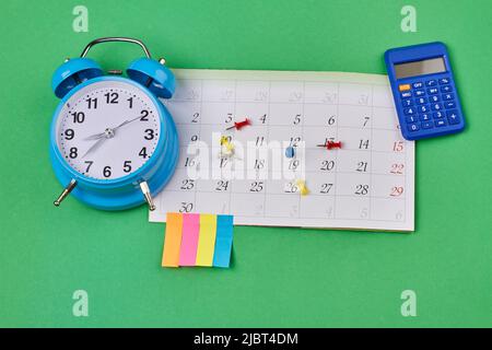 Time management and accounting concept top view flat lay. Calendar with alarm clock and calculator on green background. Stock Photo