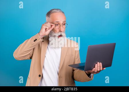 Portrait of attractive amazed grey-haired man using laptop pout lips reading report isolated over bright blue color background Stock Photo