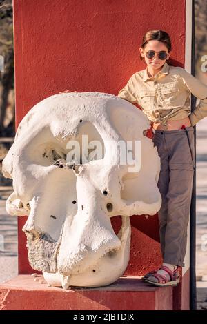 Namibia, Kunene region, Etosha National Park, At the entrance to Halali camp a young girl stands next to an African elephant skull (Loxodonta africana) Stock Photo