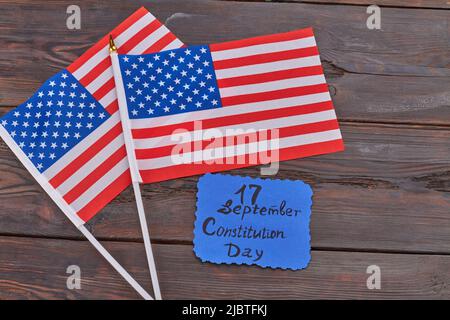 Two wave flags of the United States on woodek desk. 17 september constitution day handwritted on the card. Stock Photo