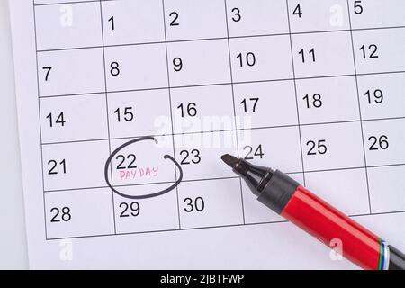 Marking pay day in the white paper calendar top view. Black non-toxic marker. Stock Photo