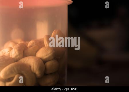 Tasty looking cashews in container. Dramatic setup. Closeup. Text space. Stock Photo