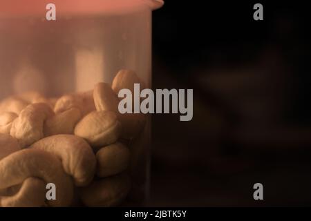 Tasty looking cashews in container. Dramatic setup. Closeup. Text space. Stock Photo