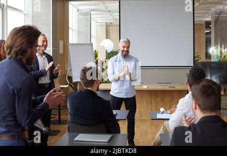Proud boss at team meeting in office applauds his subordinate congratulating him on job well done. Stock Photo