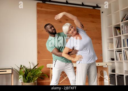 African american male physiotherapist helping caucasian senior woman to perform stretching exercise Stock Photo
