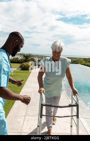 African american male health worker helping caucasian senior woman to walk with a walking frame Stock Photo