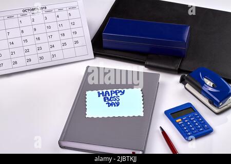 Office business stuff on white desk. Happy boss day greeting card. Book with calculator, pen etc. Stock Photo