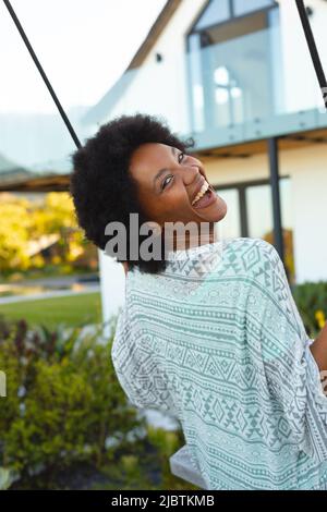 Portrait of african american woman smiling while swinging on a swing in the garden Stock Photo