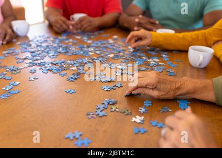 Cropped hands of multiracial seniors arranging jigsaw pieces on wooden table in nursing home Stock Photo