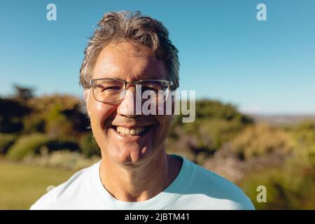 Close-up portrait of smiling caucasian senior man wearing eyeglasses against clear blue sky in yard Stock Photo