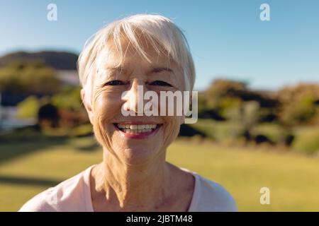 Close-up portrait of cheerful asian senior woman with short hair against clear blue sky in yard Stock Photo