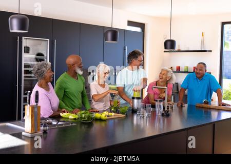 Happy multiracial senior friends talking and making smoothie on kitchen counter at retirement home Stock Photo