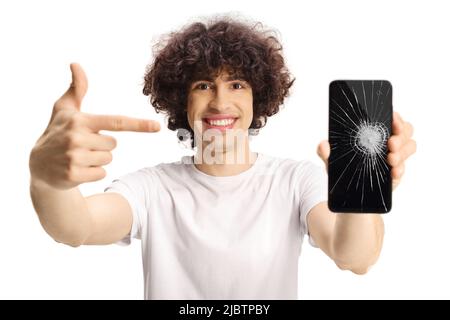 Casual young man with a dark curly hair holding a smartphone with broken screen and pointing isolated on white background Stock Photo