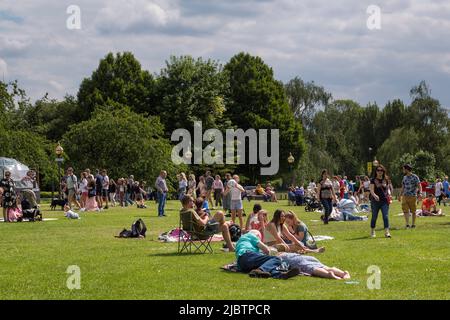 Adults and children socialise, play games and enjoy the weather in a park on a sunny day, Stock Photo