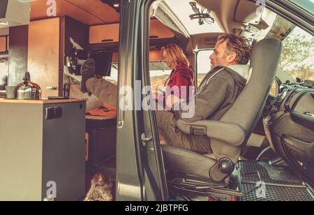 Caucasian Family Relaxing on the Seats of Their RV During a Road Trip Break. Man in His 40s Holds a TV Remote Control in His Hand Selecting a TV Progr Stock Photo
