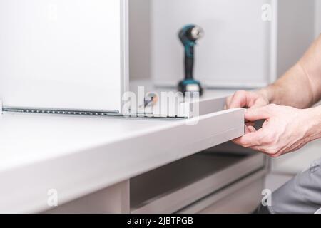 Assembling Custom Made Furniture with a Drill and Screwdriver. Attaching a Movable Desk Top to a Wall Mounted Furniture in a Room. Male Worker Making Stock Photo