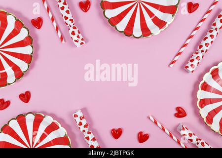 Party border with red paper plates, heart ornaments, candy and drinking straws on pink  background with copy space Stock Photo