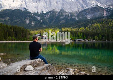 Tourist sitting on a rock and watching a beautiful view over lake Eibsee in the Bavarian Alps. Famous touristic destination in Europe Stock Photo