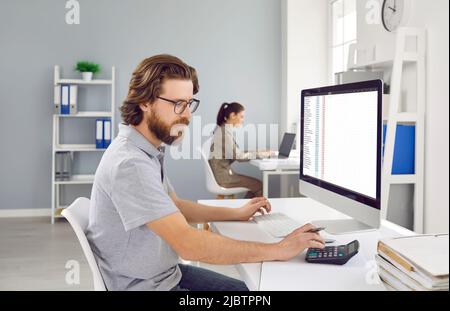 Male accountant uses calculator and software on laptop to analyze accounting finance project. Stock Photo