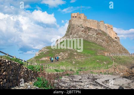 Holy Island Lindisfarne, view of people walking near the beach on Holy Island against the backdrop of Lindisfarne Castle, Northumberland, England, UK Stock Photo