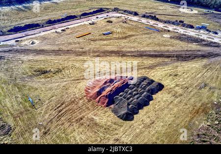 Aerial view of a construction site for the development of a new housing area with the road substructure in the back and mounds of building material in Stock Photo