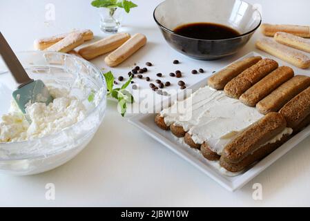 Preparing Italian tiramisu out of ladyfinger biscuits, mascarpone cheese, espresso on white table. Stock Photo