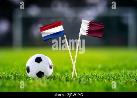 Netherlands vs. Qatar, Al Bayt, Football match wallpaper, Handmade national flags and soccer ball on green grass. Football stadium in background. Blac Stock Photo