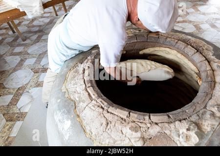 Baker placing dough into a clay oven in a bakery in Dedoplistskaro, Kakheti region Georgia eastern Europe Stock Photo