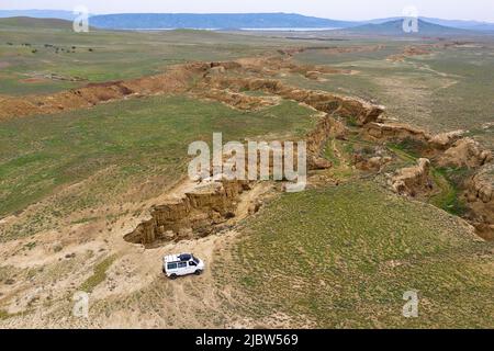 Aerial viev of Four-wheel-drive campervan driving on dirt road at small canyon on the way from Dedoplis Tskaro to Takhti-Tepha Mud Volcanoes, Georgia Stock Photo