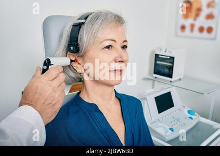 Elderly woman receives tympanometry with tympanometer probe at hearing clinic. Hearing check-up, impedance audiometry Stock Photo