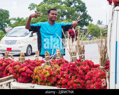 Zanzibar, Tanzania - Feb, 2021: Plenty of cluster of red lychee fruits sold directly from the car on street of Africa. Other known names: lychee, long Stock Photo