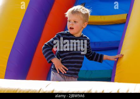 Child jumping on colorful playground trampoline. Kid jump in inflatable bounce castle on kindergarten birthday party. Activity and play center for you Stock Photo