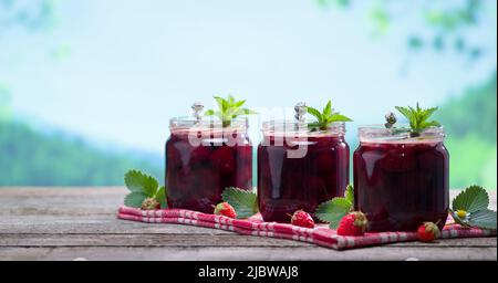 Strawberry jam jars on wooden table. Homemade delicious organic strawberry jam with nature background. Healthy breakfast concept. Stock Photo