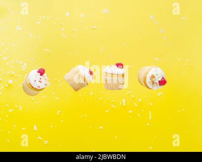 Muffins with cream and fresh raspberries in frozen flight on a bright yellow background. Festive composition. Minimalism. Birthday, holiday, sweet foo Stock Photo