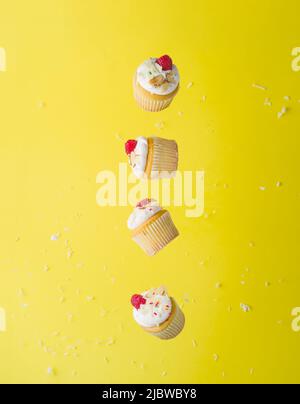 Many small muffins with whipped cream and fresh raspberries in frozen flight on a bright yellow background. Minimalism. Bright composition. Advertisin Stock Photo