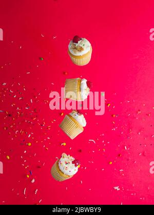 Creative composition. Delicious dessert - small muffins with cream and raspberries on a bright pink background with colored confetti in frozen flight. Stock Photo