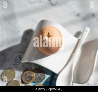 Boiled breakfast egg in an egg cup, five pound banknote and small change in the background. Stock Photo