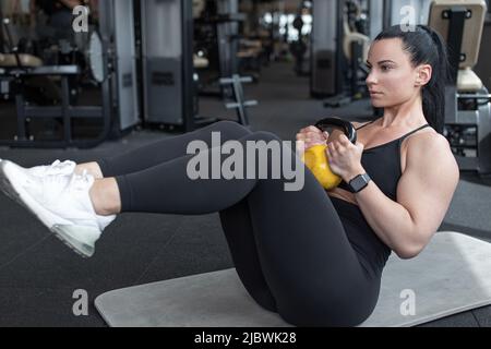Young woman doing abs workout by kettlebell in gym Stock Photo