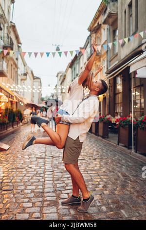 Couple in love walking in old Lviv city wearing traditional ukrainian shirts. Man raising woman, kissing and having fun outdoors on street Stock Photo