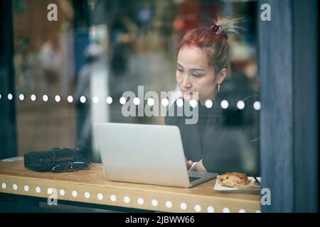 through glass shot of a mid adult asian businesswoman working in coffee shop using laptop computer Stock Photo