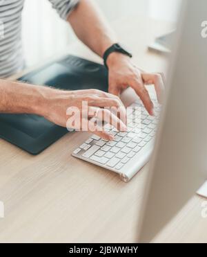 Writer typing modern computer keyboard writing novel sitting at the white wood table. Distance or freelance work on worldwide quarantine time concept Stock Photo