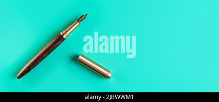 Wooden and gold fountain ink pen, opened, cap on the right, blue green background top down view, space for text Stock Photo