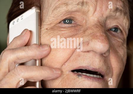 Elderly senior woman holding gold coloured phone next to her ear, talking - closeup detail Stock Photo