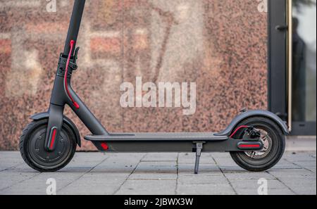 Electric scooter parked on tiled pavement - closeup detail, marble wall and glass door background Stock Photo