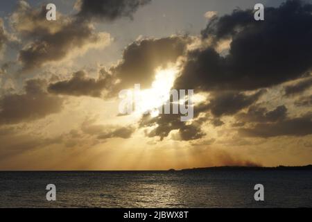 Bahama Sunset - A fire burns on the island below a beautiful sunset with sunrays exploding from behind some perfectly sun obstructing clouds. Stock Photo