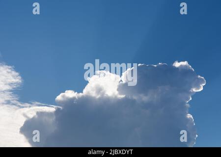 A big rain cloud and the sun rays break through behind the clouds on a summer day. Close up and copy space for text or design Stock Photo