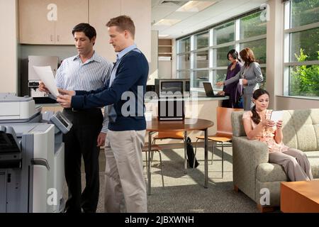Two coworkers talking at printer while in breakroom at office. Stock Photo