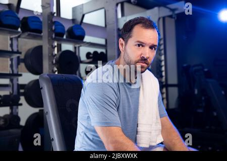 Male personal trainer sitting on weight bench after training client finish in a gym Stock Photo