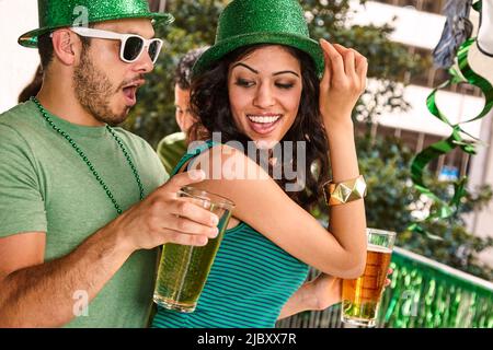 Young diverse couple dancing together wearing green sparkle hats and holding beer glasses for St. Patrick's Day. Stock Photo